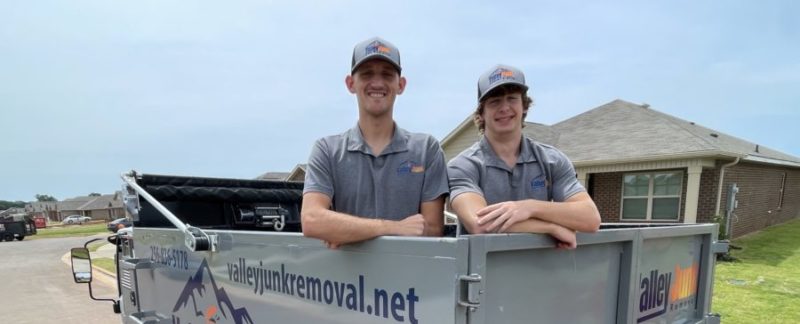 junk removal pros smiling in the bed of truck